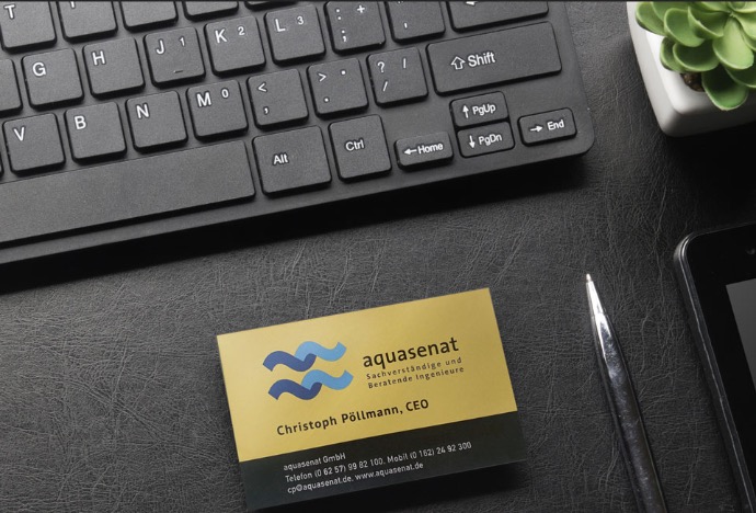 aquasenat business card bird's eye view of a black leather look desk with a black keyboard, a cut cactus, and a golden business card